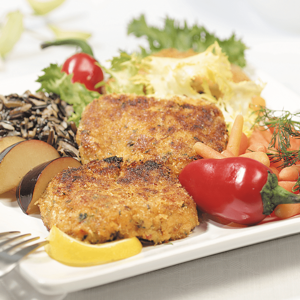 Two Dungeness crab cakes served on a white plate, garnished with fresh herbs and lemon slices.
